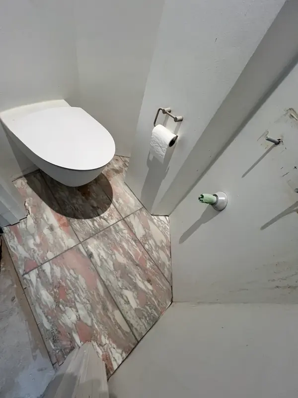 Marmorgulvet lagt op omkring et vægophængt toilet i et smalt toiletrum, hvor væggene endnu står ubehandlede